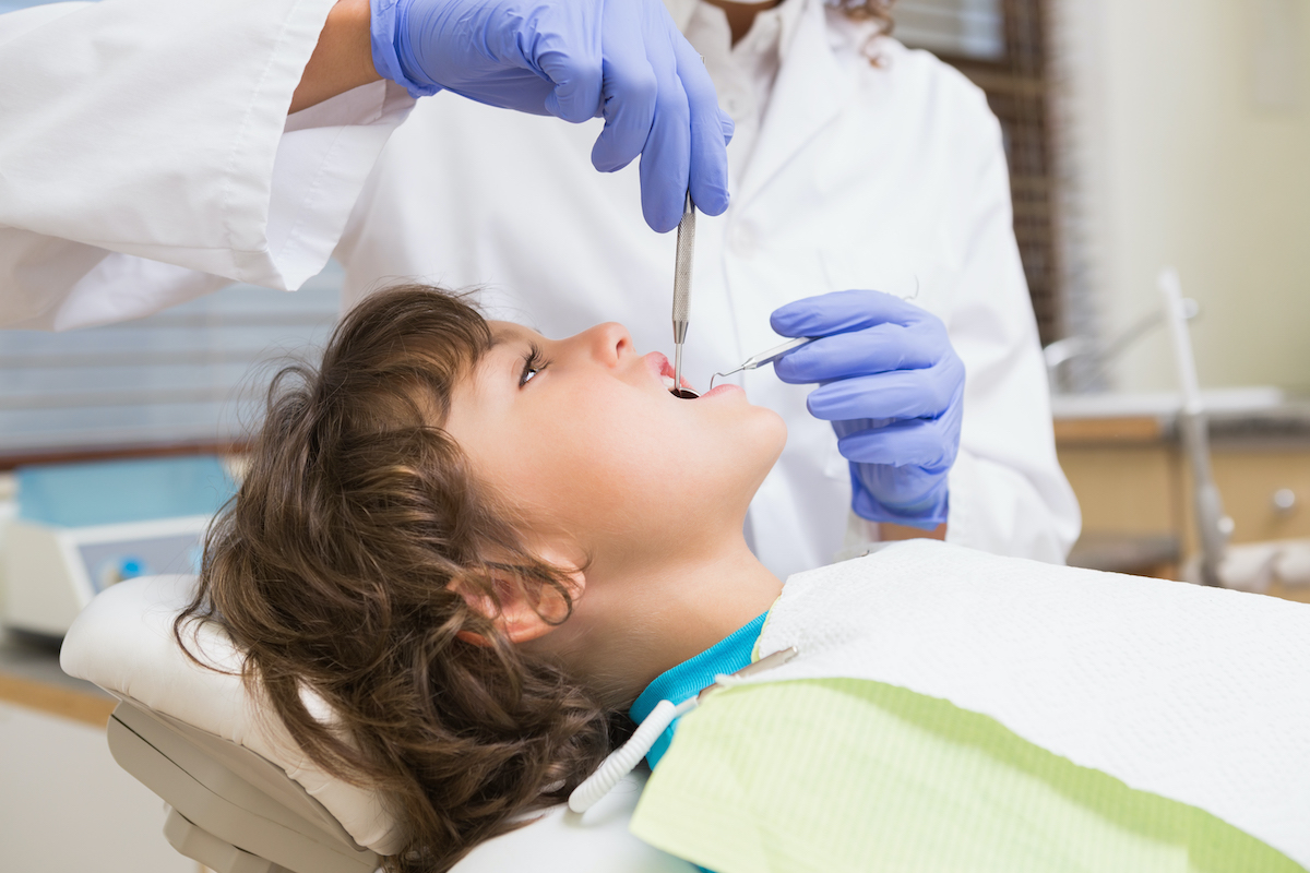 Pediatric dentist examining a little boys teeth in the dentists chair at the dental clinic