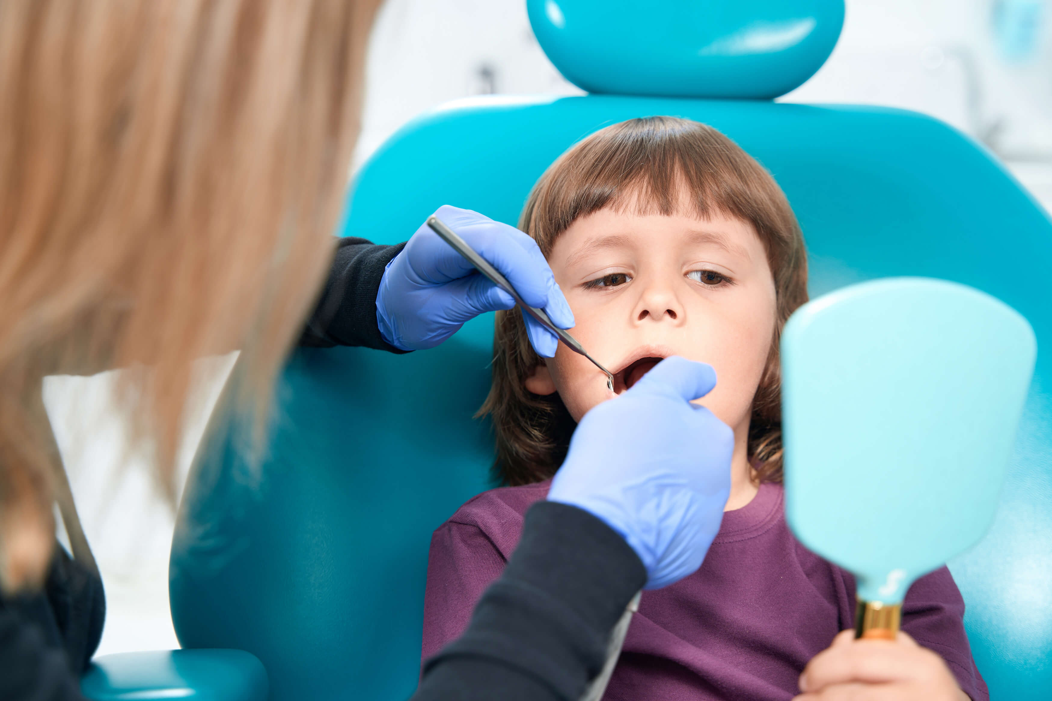 Side view portrait of dentist treating teeth of cute little girl sitting in dental chair, filling cavities and doing professional cleaning