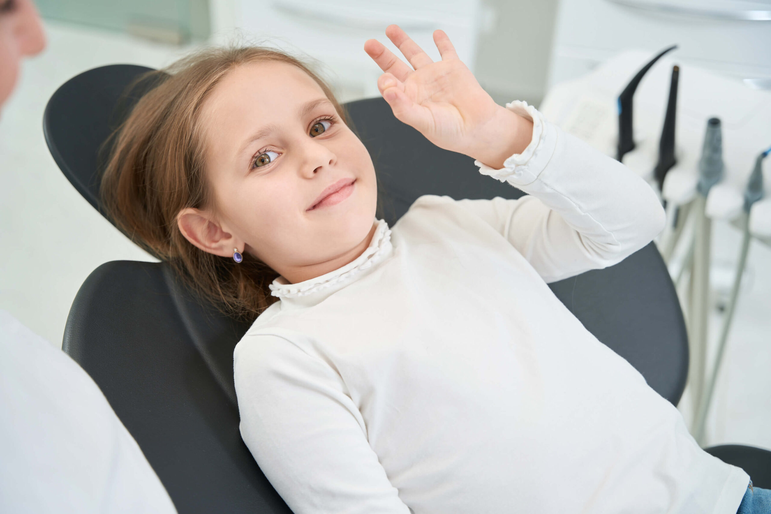 young girl waving and sitting in a pediatric dentist office
